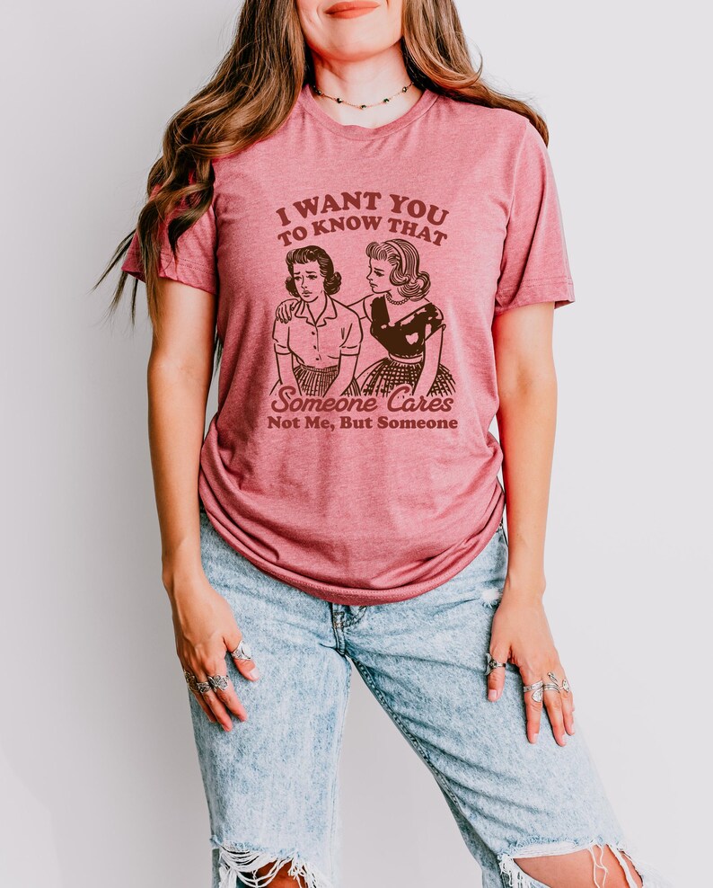 Op de afbeelding: Een roze T-shirt met de tekst "Ik wil dat je weet dat iemand geeft, niet ik, maar iemand" en een retro-illustratie van twee vrouwen.