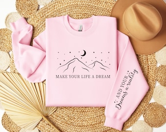 Może przedstawiać: Różowa bluza z czarnym nadrukiem gór i tekstem "Make your life a dream". Rękawy mają napis "...and your dreams a reality".