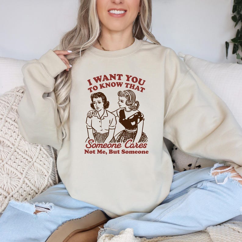 Op de afbeelding: Een beige sweatshirt met een vintage-stijl afbeelding van twee vrouwen. De tekst op het sweatshirt luidt "I want you to know that someone cares not me, but someone."