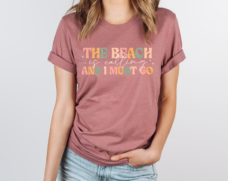May include: A mauve t-shirt with the text "THE BEACH is calling AND I MUST GO" in colorful letters.