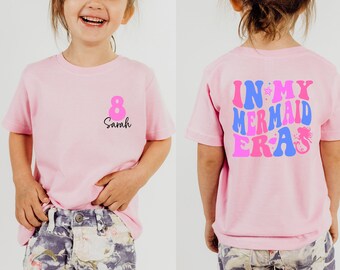 Peut inclure: T-shirt rose avec l'inscription "IN MY MERMAID ERA" au dos. Le devant affiche le chiffre 8 et le prénom "Sarah". Le design est destiné à un enfant.