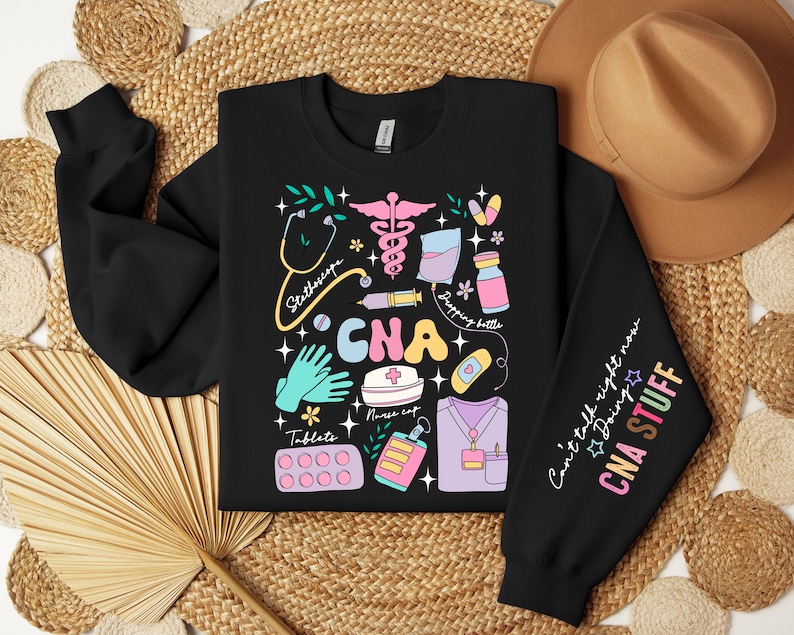 May include: Black sweatshirt with a colorful graphic design of medical tools and the text "CNA" on the front. The right sleeve has the text "Can't talk right now doing CNA STUFF".