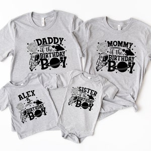 May include: Set of four grey t-shirts with black astronaut and planet designs. The shirts say "Daddy of the Birthday Boy", "Mommy of the Birthday Boy", "Sister of the Birthday Boy", and "Alex 5 Birthday Boy".
