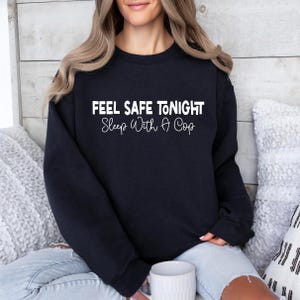 May include: A black sweatshirt with the text "Feel Safe Tonight Sleep With A Cop" in white lettering.