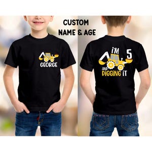 May include: Black t-shirt with a yellow and white construction vehicle graphic. The front of the shirt says "GEORGE" under the vehicle. The back of the shirt says "I'M 5 AND DIGGING IT". The text "CUSTOM NAME & AGE" is above the front of the shirt.