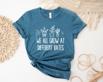 May include: Teal blue t-shirt with a white graphic of potted plants and the text "We all grow at different rates".