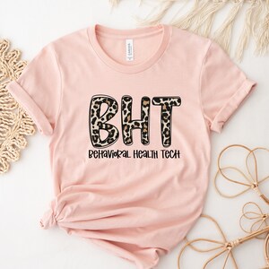 May include: Pink t-shirt with a leopard print design that says "BHT Behavioral Health Tech" in black text.
