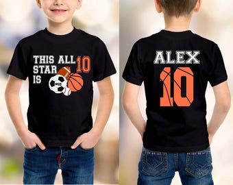 Może przedstawiać: Czarny t-shirt z napisem "THIS ALL STAR IS 10" i grafiką piłek sportowych. Tył koszulki ma imię "ALEX" i numer "10" w kolorze pomarańczowym. Koszulka jest noszona przez dziecko.