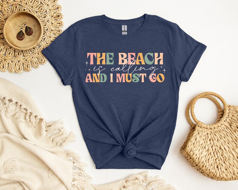 May include: A navy blue t-shirt with the text "THE BEACH is calling AND I MUST GO" in colorful, retro-style lettering.