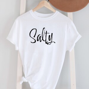 May include: White t-shirt with the word "Salty" written in black cursive script.