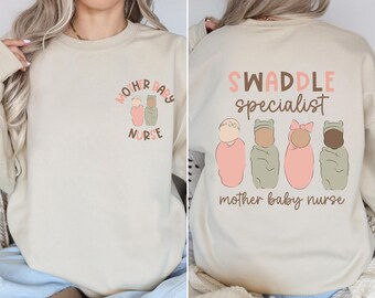 May include: A beige sweatshirt with the text "Mother Baby Nurse" on the front and "Swaddle specialist mother baby nurse" on the back. The front design features two cartoon babies in swaddles. The back design features four cartoon babies in swaddles.