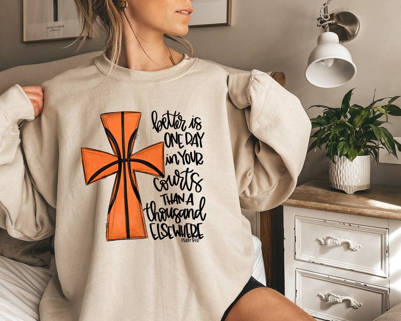 May include: A beige sweatshirt with a basketball-shaped cross graphic and the text "better is one day in your courts than a thousand elsewhere Psalm 84:10".