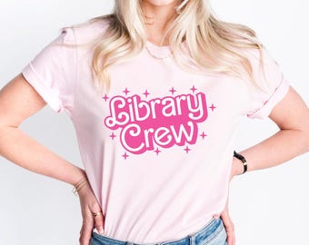 May include: A pink t-shirt with the text "Library Crew" in pink with white outlines and white stars around the text.