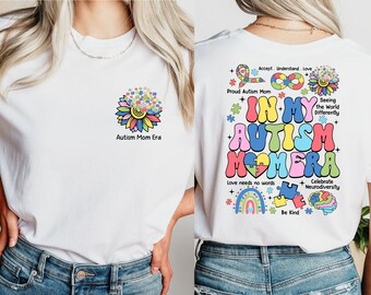 May include: White t-shirt with a colorful flower design made of puzzle pieces. The text "Autism Mom Era" is printed below the flower. The back of the shirt has a colorful design with the text "In My Autism Mom Era" and other phrases like "Love Needs No Words" and "Celebrate Neurodiversity".