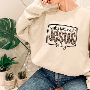 Può includere: Una felpa beige con una grafica nera che dice "only talking to Jesus today" con un design a stampa leopardata.