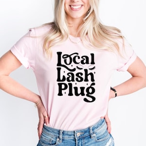 May include: A pink t-shirt with the text "Local Lash Plug" in black, featuring stylized eyelashes and glitter accents.