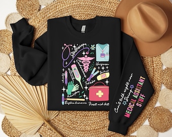 May include: Black sweatshirt with a colorful graphic print of medical supplies and the text "Can't talk right now Doing MEDICAL ASSISTANT STUFF".