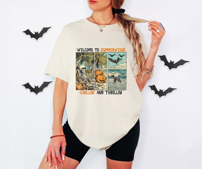 May include: Cream-colored t-shirt with a graphic that reads "WELCOME TO SUMMERWEEN!" and "CHILLIN AND THRILLIN". The graphic features a skeleton, pumpkins, bats, and a beach scene. Black shorts are also visible.