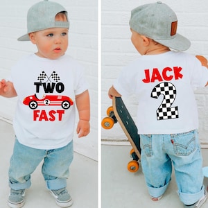 May include: A toddler wearing a white t-shirt with a red race car graphic and the words "TWO FAST" in red. The child is also wearing a gray baseball cap and blue jeans. The back of the shirt has the name "JACK" and the number "2".