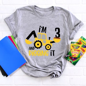 May include: A gray t-shirt with a yellow construction vehicle graphic and the text "I'm 3 and digging it".