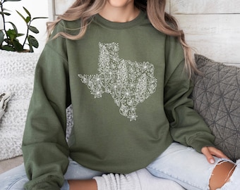 May include: A green sweatshirt with a white outline of the state of Texas made up of flowers. The sweatshirt is being worn by a person.