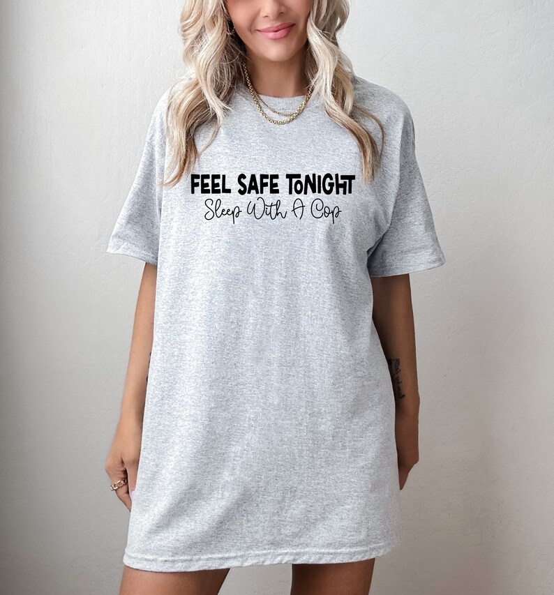 Puede incluir: Camiseta gris de gran tama&ntilde;o con el texto "Feel Safe Tonight Sleep With A Cop" impreso en negro.