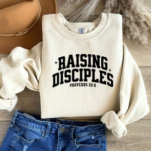May include: A cream-colored sweatshirt with black text that reads "Raising Disciples" and "Proverbs 22:6".