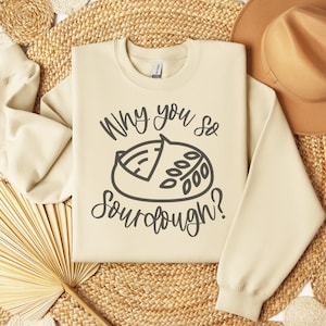 May include: A beige sweatshirt with the text "Why you so sourdough?" and a black and white illustration of a loaf of sourdough bread.