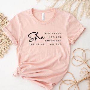 May include: A pink t-shirt with the text "She motivates, inspires, empowers. She is me. I am she."