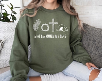 May include: A green sweatshirt with a white graphic of a palm branch, a crown of thorns, a cross, and a tomb. The text "A lot can happen in 7 days" is below the graphic.