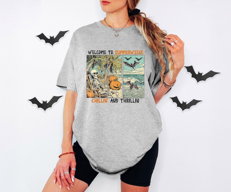 May include: A gray t-shirt with a graphic that reads "WELCOME TO SUMMERWEEN! CHILLIN AND THRILLIN." The graphic features a skeleton on a beach, pumpkins, bats, and ocean waves. Black shorts are worn.