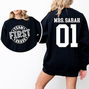 May include: Black sweatshirt with white text that says "Team First Grade" on the front and "Mrs. Sarah 01" on the back.