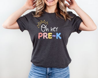Peut inclure: Un t-shirt gris foncé avec un graphique de soleil jaune et le texte "Oh hey PRE-K" en lettres colorées.