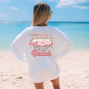 Può includere: Felpa bianca con grafica rosa e rossa di un furgone vintage con tavole da surf, con la scritta "Sea Ya! Salty Beach". Il design evoca un tema di vacanza al mare.