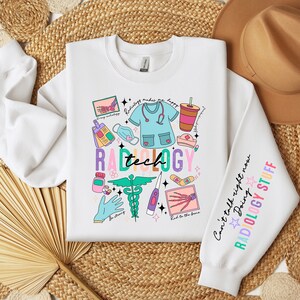 May include: White sweatshirt with a colorful graphic design featuring the words "Radiology Tech" and various medical illustrations. The sleeve has the text "Can't talk right now Doing RADIOLOGY STUFF".