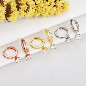 May include: Five pairs of hoop earrings with a dangling crystal. The hoops are available in gold, silver, and rose gold.