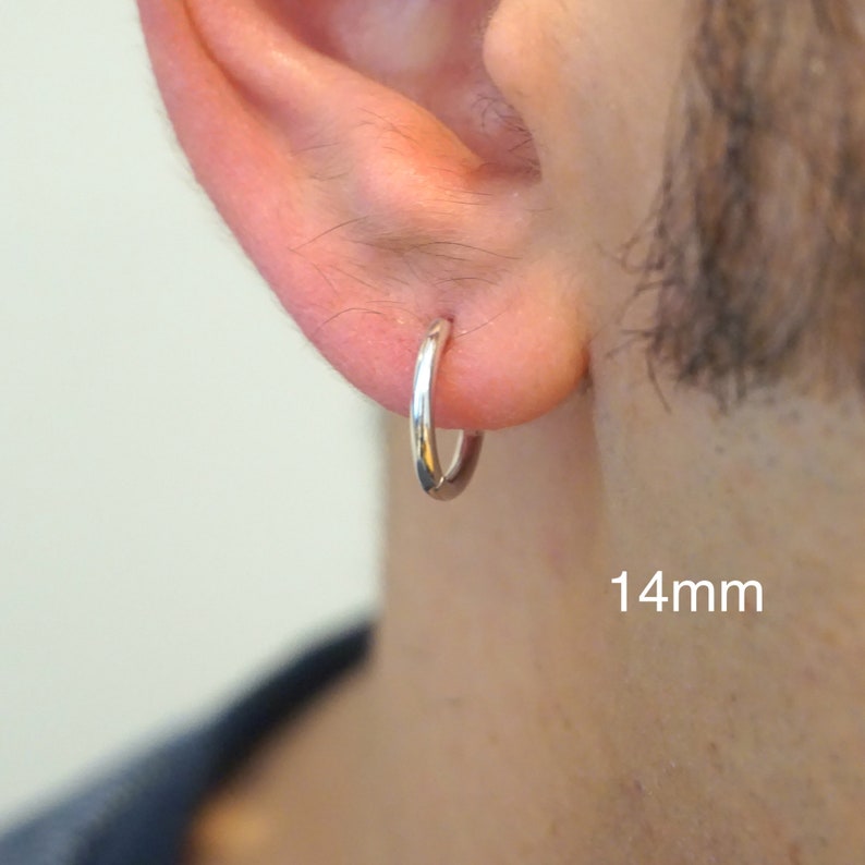 May include: A small, polished silver-colored hoop earring worn in the earlobe. The earring has a circular, continuous design with a smooth, reflective metallic finish. The text 14mm is clearly visible in the lower right corner of the image.