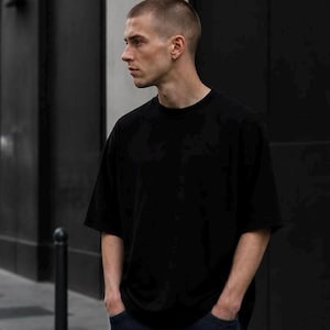 May include: A solid black short-sleeved t-shirt with a crew neckline and a relaxed, loose-fitting silhouette. The garment is made of a plain, opaque fabric and features a simple, unadorned design with standard hemmed sleeves and a straight bottom hem.