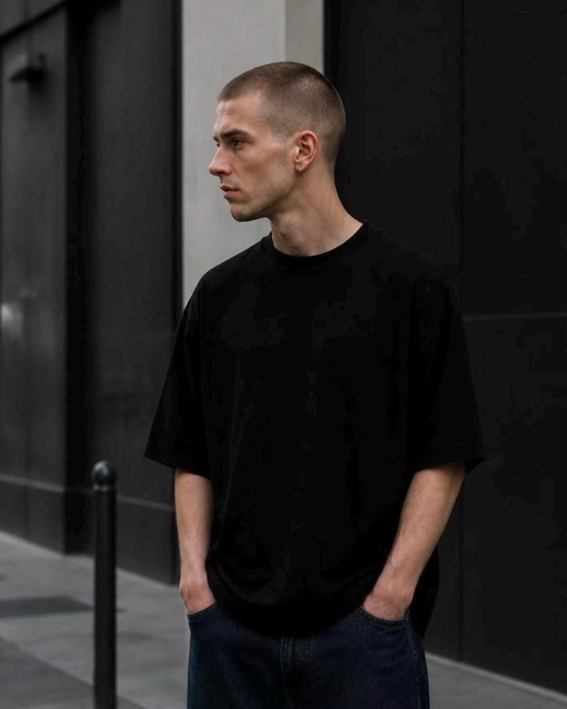 May include: A solid black short-sleeved t-shirt with a crew neckline and a relaxed, loose-fitting silhouette. The garment is made of a plain, opaque fabric and features a simple, unadorned design with standard hemmed sleeves and a straight bottom hem.