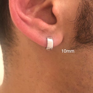 Könnte beinhalten: Ein silberner Ohrring mit einem Durchmesser von 10 mm. Der Ohrring wird am linken Ohr einer Person getragen.