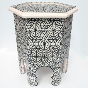Puede incluir: Mesa auxiliar octogonal con un patrón geométrico en blanco y negro. La mesa tiene tres patas con un diseño curvo.