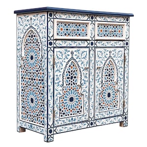 Può includere: Un mobile bianco con intricati motivi geometrici blu e arancioni. Il mobile ha due cassetti e due ante, con un top e finiture blu scuro. Il design ricorda l'arte marocchina o islamica, con uno stile ornato.