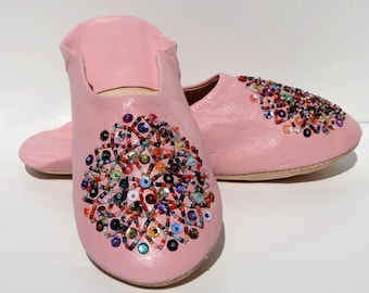 May include: A pair of pink leather slippers with colorful beaded embellishments. The slippers have a pointed toe and a flat sole.