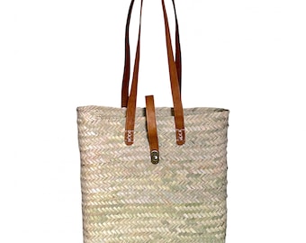 May include: A woven straw tote bag with brown leather straps and a buckle closure. The bag has a natural, light brown color.