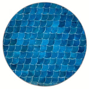 Puede incluir: Tablero de mesa redondo con diseño de mosaico. La superficie está cubierta de pequeñas baldosas azules en forma de escamas, creando un patrón texturizado. Las baldosas varían en tonos de azul, de claro a oscuro, y están delineadas con lechada blanca.