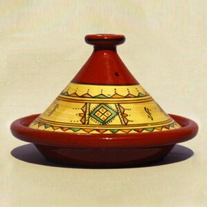 May include: A red ceramic tagine with a yellow and green geometric design. The tagine has a domed lid and a wide base.