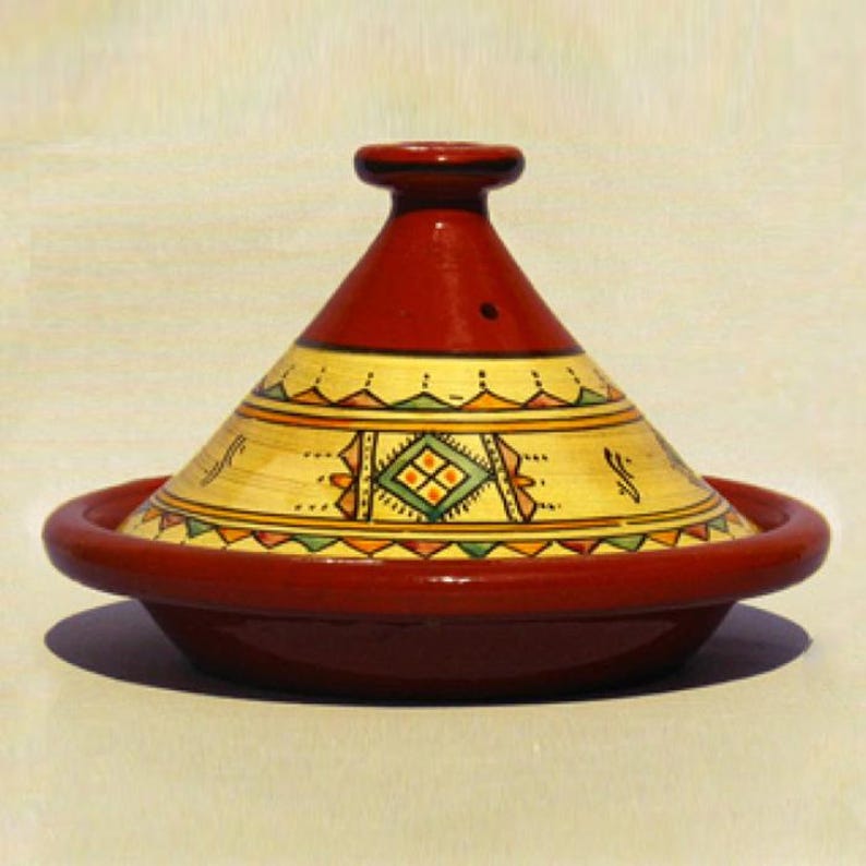 May include: A red ceramic tagine with a yellow and green geometric design. The tagine has a domed lid and a wide base.