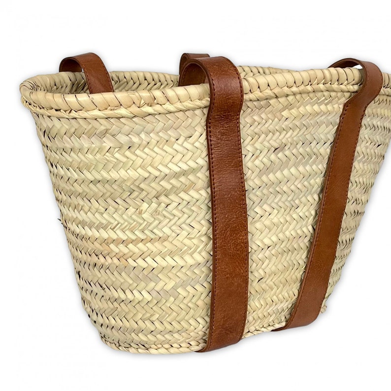 May include: A large, woven straw tote bag with two brown leather straps. The bag is made of natural straw and has a herringbone pattern.