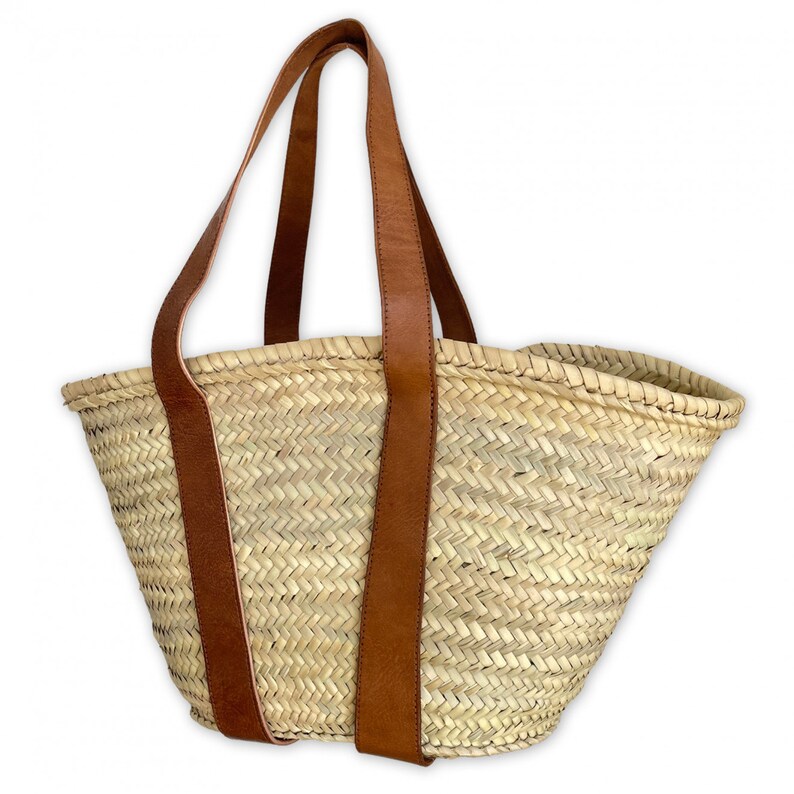 May include: A woven straw tote bag with brown leather handles. The bag is a light beige colour and has a woven pattern.