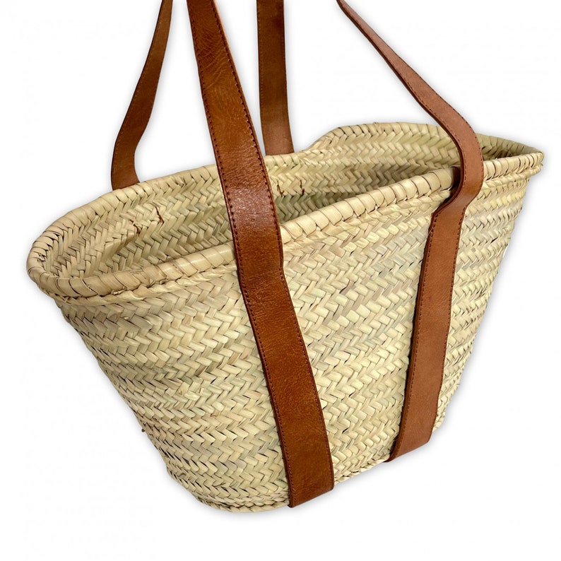 May include: A large, woven straw tote bag with brown leather handles. The bag is made of a natural, light brown straw and has a wide, open top.